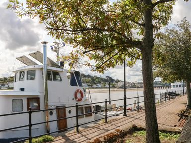 A riverside walkway with trees benches and docked boats at Barley Bay near Hartland