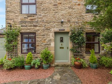 Exterior of a stone cottage with a green front door and potted plants at Crescent Cottage in Haltwhistle near Hadrians Wall