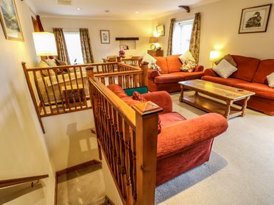 A living room with red sofas wooden coffee table and dining table with chairs at Crescent Cottage in Haltwhistle near Hadrians Wall