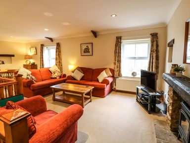A living room with red sofas a wooden coffee table a TV on a stand and windows with patterned curtains at Crescent Cottage in Haltwhistle near Hadrians Wall
