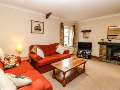A living room with red sofas wooden coffee table television and fireplace at Crescent Cottage in Haltwhistle near Hadrians Wall