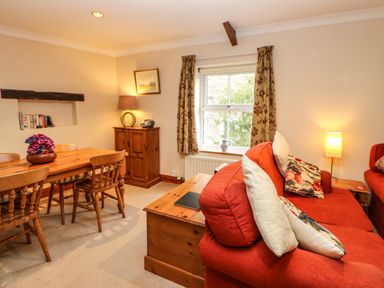 A living room with a wooden dining table and chairs red sofas and a window with floral curtains at Crescent Cottage in Haltwhistle near Hadrians Wall