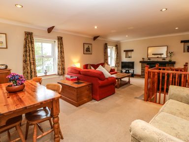 A living room with red and beige sofas a wooden dining table and chairs a TV and a fireplace at Crescent Cottage in Haltwhistle near Hadrians Wall