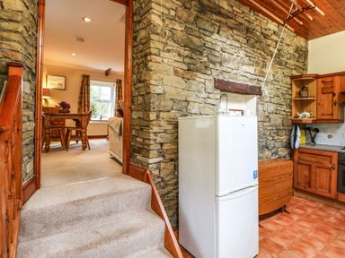 A kitchen area with a white refrigerator stone walls wooden cabinets and a view into a dining room at Crescent Cottage Haltwhistle near Hadrian's Wall