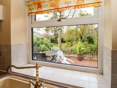 A kitchen sink with a brass faucet below a window showing an outdoor patio with plastic and wooden chairs and a garden at Crescent Cottage Haltwhistle near Hadrians Wall