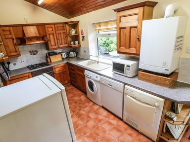A kitchen with wooden cabinets appliances and a window overlooking a garden at Crescent Cottage in Haltwhistle near Hadrian's Wall