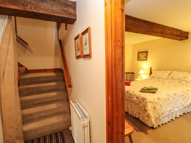 A carpeted staircase next to a bedroom with a double bed and a bedside table with lamp at Crescent Cottage in Haltwhistle near Hadrians Wall