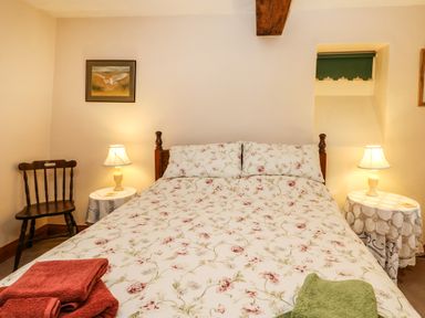 A bedroom with a double bed floral bedspread two side tables with lamps and a wooden chair at Crescent Cottage in Haltwhistle near Hadrians Wall