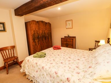 A bedroom with a floral bedspread wooden chairs a wooden wardrobe and a chest of drawers at Crescent Cottage in Haltwhistle near Hadrians Wall