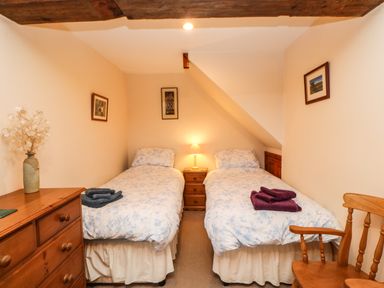 A bedroom with two single beds a wooden dresser and a wooden chair at Crescent Cottage in Haltwhistle near Hadrians Wall
