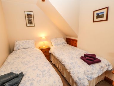 A bedroom with two single beds and floral bedding a small wooden nightstand with a lamp and folded towels on the beds at Crescent Cottage in Haltwhistle near Hadrians Wall