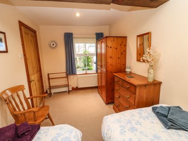 A bedroom with two single beds a wooden chair wooden wardrobe and chest of drawers at Crescent Cottage in Haltwhistle near Hadrians Wall