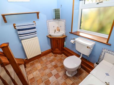 A bathroom with a toilet, corner sink with wooden cabinet, towel rail with striped towel, window and tiled floor at Crescent Cottage in Haltwhistle near Hadrians Wall