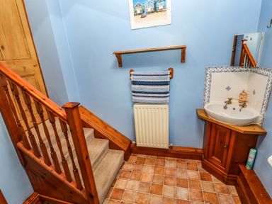 A staircase with wooden banister next to a sink with cabinet in a blue walled room at Crescent Cottage in Haltwhistle near Hadrian's Wall