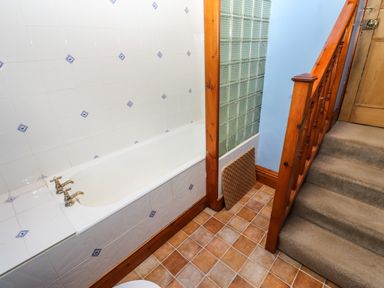 A bathroom with a tiled bathtub next to a wooden staircase with carpet at Crescent Cottage in Haltwhistle near Hadrians Wall