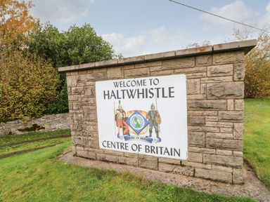 A stone sign welcoming to Haltwhistle centre of Britain with trees and grass around Crescent Cottage in Haltwhistle near Hadrians Wall