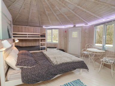 A bedroom with a double bed and bunk beds wooden walls a small table and two chairs at Spekes Mill near Hartland