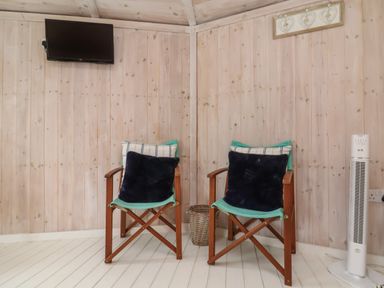 Two wooden chairs with cushions against a wooden paneled wall with a wall mounted tv and a white tower fan at Spekes Mill near Hartland