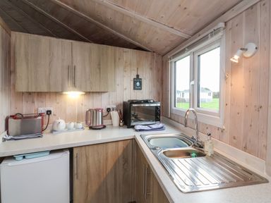 A small kitchen with wooden cabinets countertop with toaster kettle teapot microwave and a window at Spekes Mill near Hartland