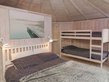 A bedroom with a double bed and bunk beds with patterned bedding under a wooden ceiling at Spekes Mill near Hartland