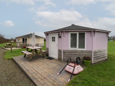 Two small octagonal cabins with picnic tables on wooden decks and a wheelbarrow on the deck at Spekes Mill near Hartland