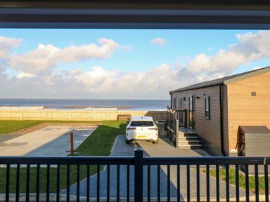 A view of a driveway with a white car parked next to a wooden lodge facing the sea at The Sea Lodge in Bacton near Walcott
