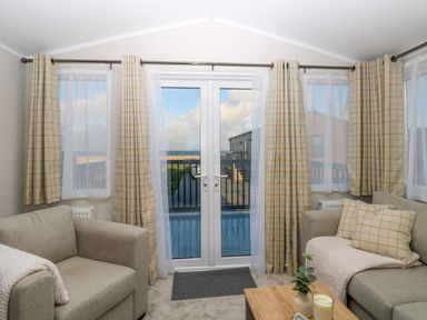 A living room with two sofas a small wooden table and glass doors with curtains at The Sea Lodge in Bacton near Walcott