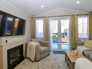 A living room with armchairs a coffee table a wall-mounted television and glass doors leading to a balcony at The Sea Lodge in Bacton near Walcott