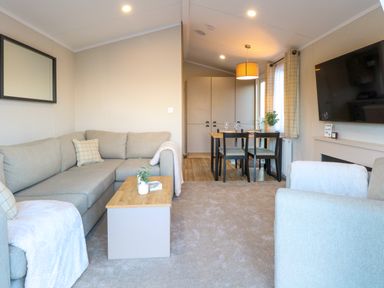 A living room with a beige sectional sofa, coffee table, dining table with four chairs, and a wall-mounted TV at The Sea Lodge in Bacton near Walcott