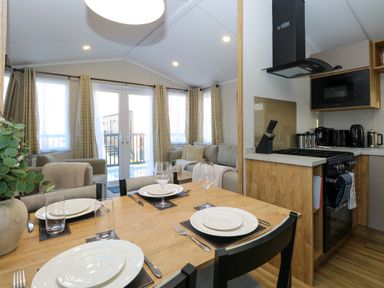 A dining table set with plates and glasses in an open plan living area with a kitchen and sofa at The Sea Lodge in Bacton near Walcott