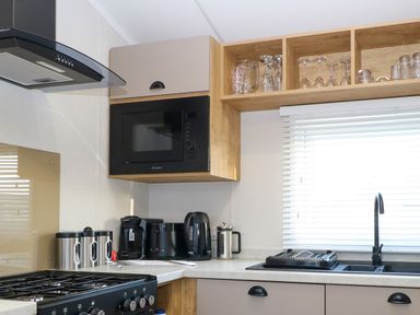 A kitchen corner with a stove microwave coffee machine electric kettle and a sink with a drying rack at The Sea Lodge in Bacton near Walcott