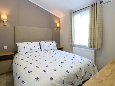 A bedroom with a double bed featuring sea-themed bedding bedside tables wall lights and a window with curtains at The Sea Lodge in Bacton near Walcott