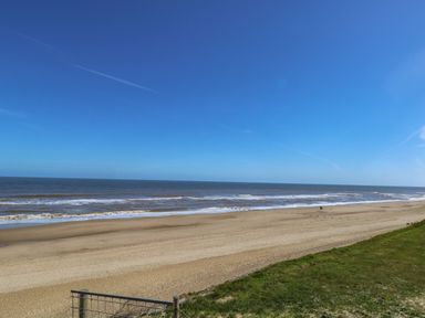 A sandy beach with waves and blue sky at The Sea Lodge in Bacton near Walcott