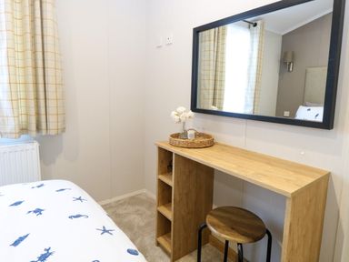 A bedroom corner with a wooden desk a round stool a wall mirror and a bed with sea-themed bedding at The Sea Lodge in Bacton near Walcott