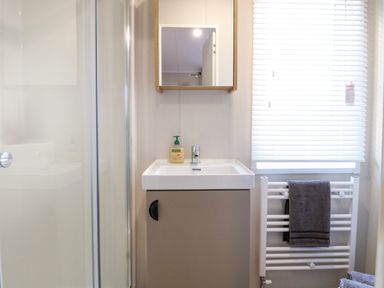 A bathroom with a sink cabinet mirror soap dispenser shower and towel rail at The Sea Lodge in Bacton near Walcott