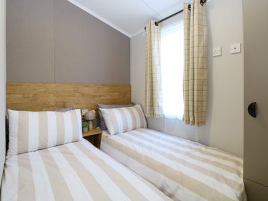 A bedroom with two single beds with striped bedding and a window with checked curtains at The Sea Lodge in Bacton near Walcott