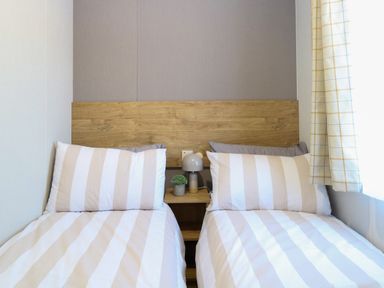 A bedroom with two single beds with striped bedding and a wooden headboard at The Sea Lodge in Bacton near Walcott