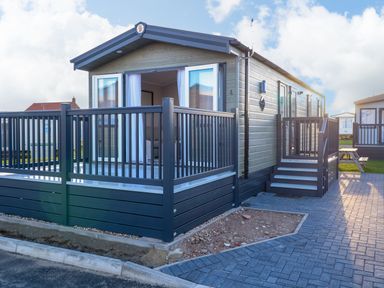 An exterior view of a mobile home with a blue deck and stairs on a paved area at The Sea Lodge in Bacton near Walcott