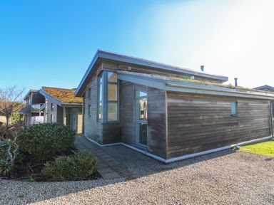 A wooden house with large windows and gravel pathway surrounded by shrubs at Una Lodge 77 in Carbis Bay
