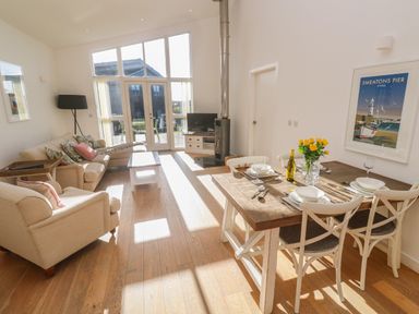 A living room with dining table set with plates and glasses and a sofa set near large windows at Una Lodge 77 in Carbis Bay