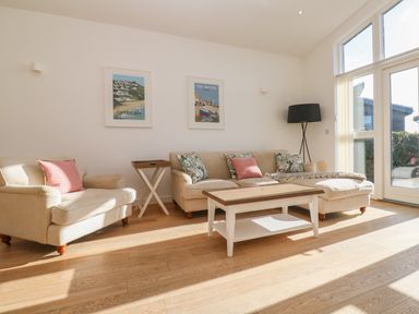 A living room with beige sofas a wooden coffee table paintings on the wall and large windows at Una Lodge 77 in Carbis Bay