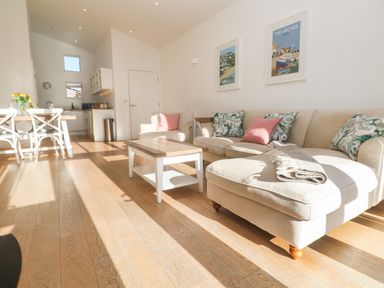 A living room with beige sofas pink and patterned cushions a wooden coffee table and a dining table with chairs at Una Lodge 77 in Carbis Bay