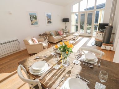A dining table set with plates and glasses and a living room with sofas and a wood stove at Una Lodge 77 in Carbis Bay