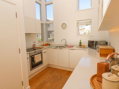 A kitchen with white cabinets wooden floor and countertop with a sink oven microwave and various kitchen items at Una Lodge 77 in Carbis Bay