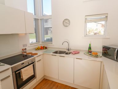 A kitchen with white cabinets a double sink a stove oven microwave and fruit on the counter at Una Lodge 77 in Carbis Bay