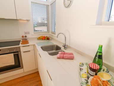 A kitchen countertop with a sink a bottle and food items in a tray and a fruit platter near windows at Una Lodge 77 in Carbis Bay
