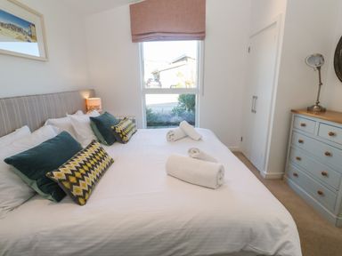 A bedroom with a bed with pillows and rolled towels next to a window and a chest of drawers with a lamp at Una Lodge 77 in Carbis Bay