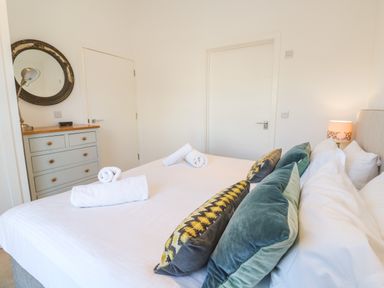 A bedroom with a bed with pillows and rolled towels a dresser with a mirror and a lamp at Una Lodge 77 in Carbis Bay