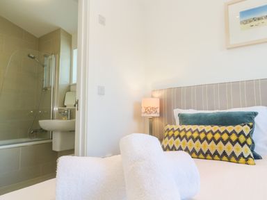 A bedroom with a bed with pillows and towels next to a bathroom with a shower at Una Lodge 77 in Carbis Bay