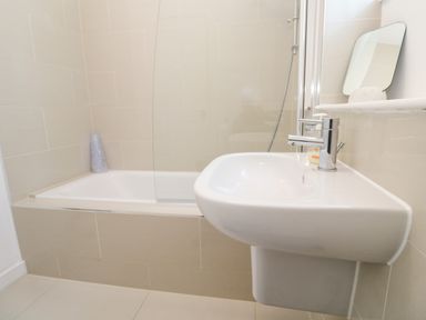 A bathroom with a bathtub shower and a wall mounted sink at Una Lodge 77 in Carbis Bay
